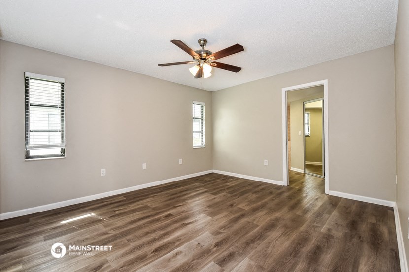 the spacious living room with hardwood flooring and a ceiling fan