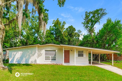 a small white house with a red door in a yard with trees