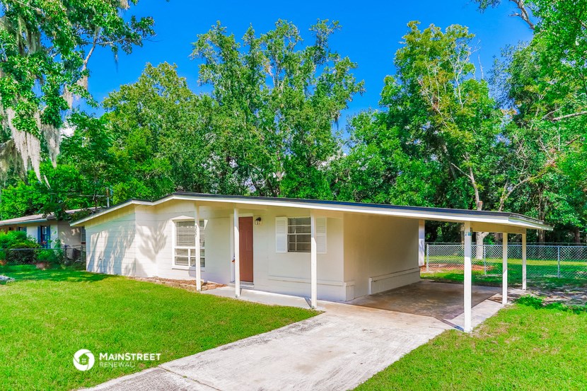 a small white house with a driveway and a yard with trees