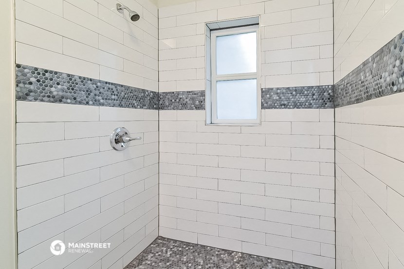 a white tiled bathroom with a shower and a window