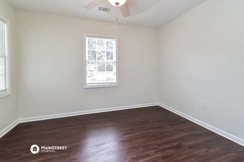 a bedroom with white walls and wood flooring and a window