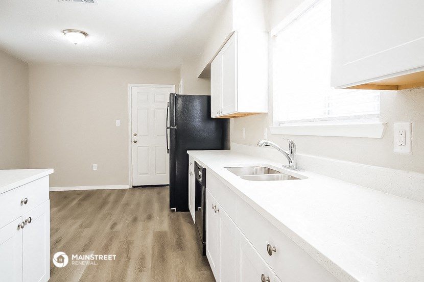 an empty kitchen with white cabinets and a black refrigerator