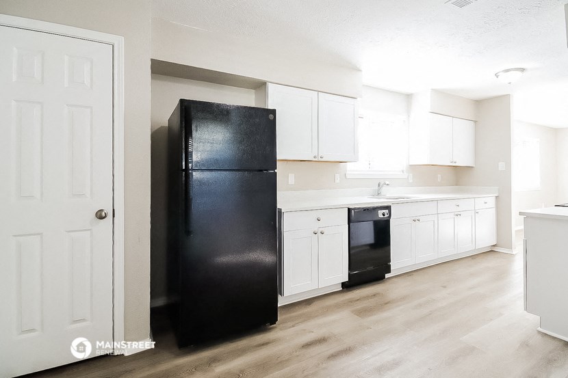 an empty kitchen with white cabinets and a black refrigerator