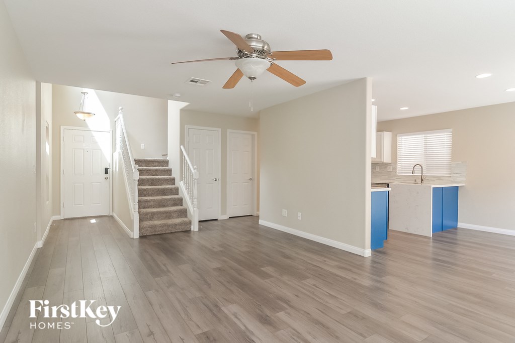 an empty living room with a ceiling fan and a staircase