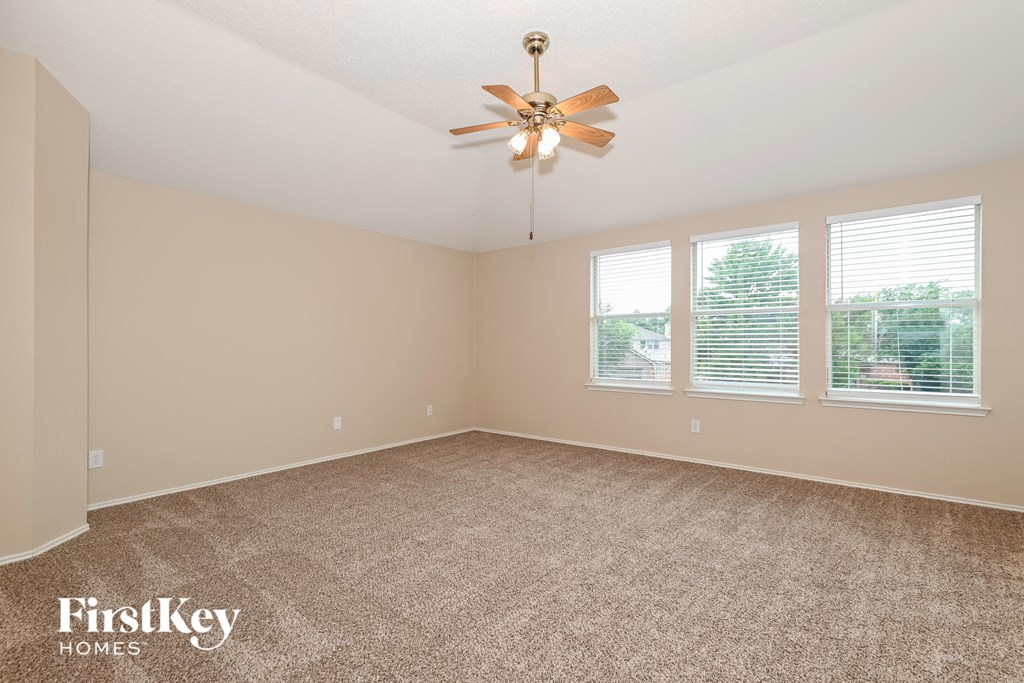an empty living room with a ceiling fan and three windows