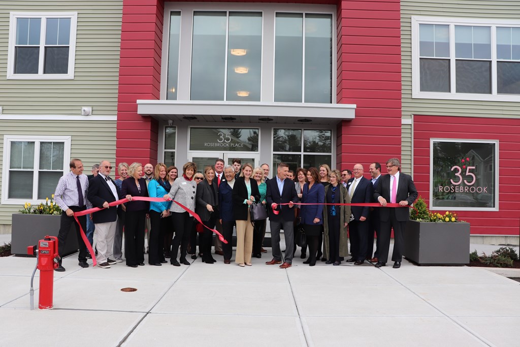 a group of people cutting a red ribbon in front of a building