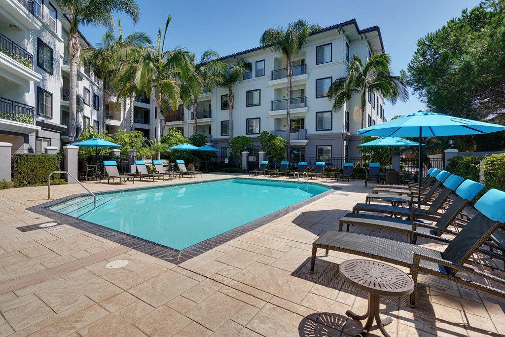 a swimming pool with chairs and umbrellas in front of an apartment building