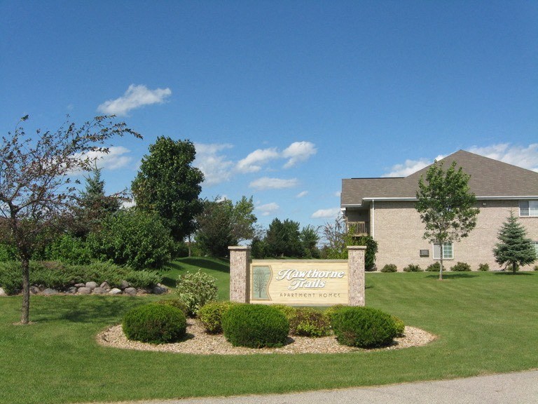 a sign in front of a building with a lawn and trees