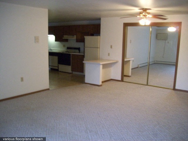 an empty living room with a kitchen and a ceiling fan
