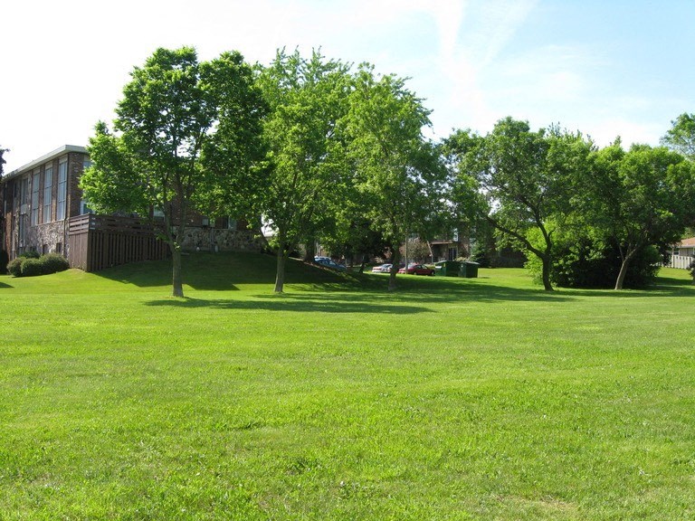 a large grass field with trees in front of a building