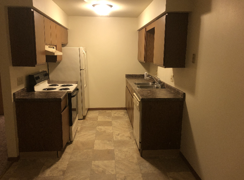 A kitchen with a white refrigerator, black countertops, and brown cabinets.