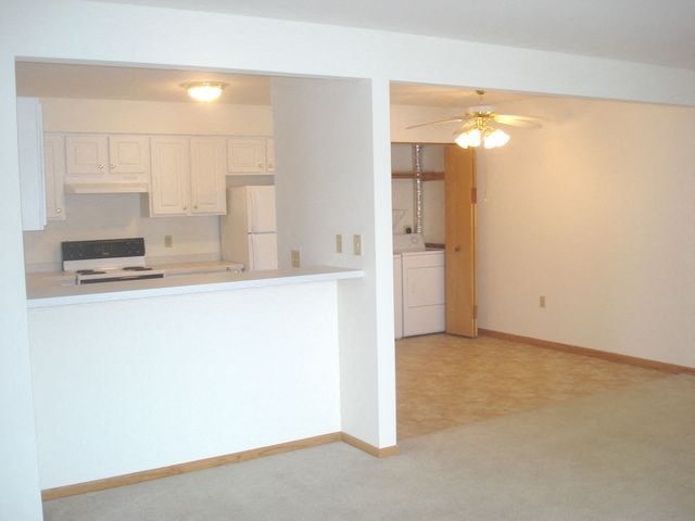 an empty living room with a kitchen and a ceiling fan