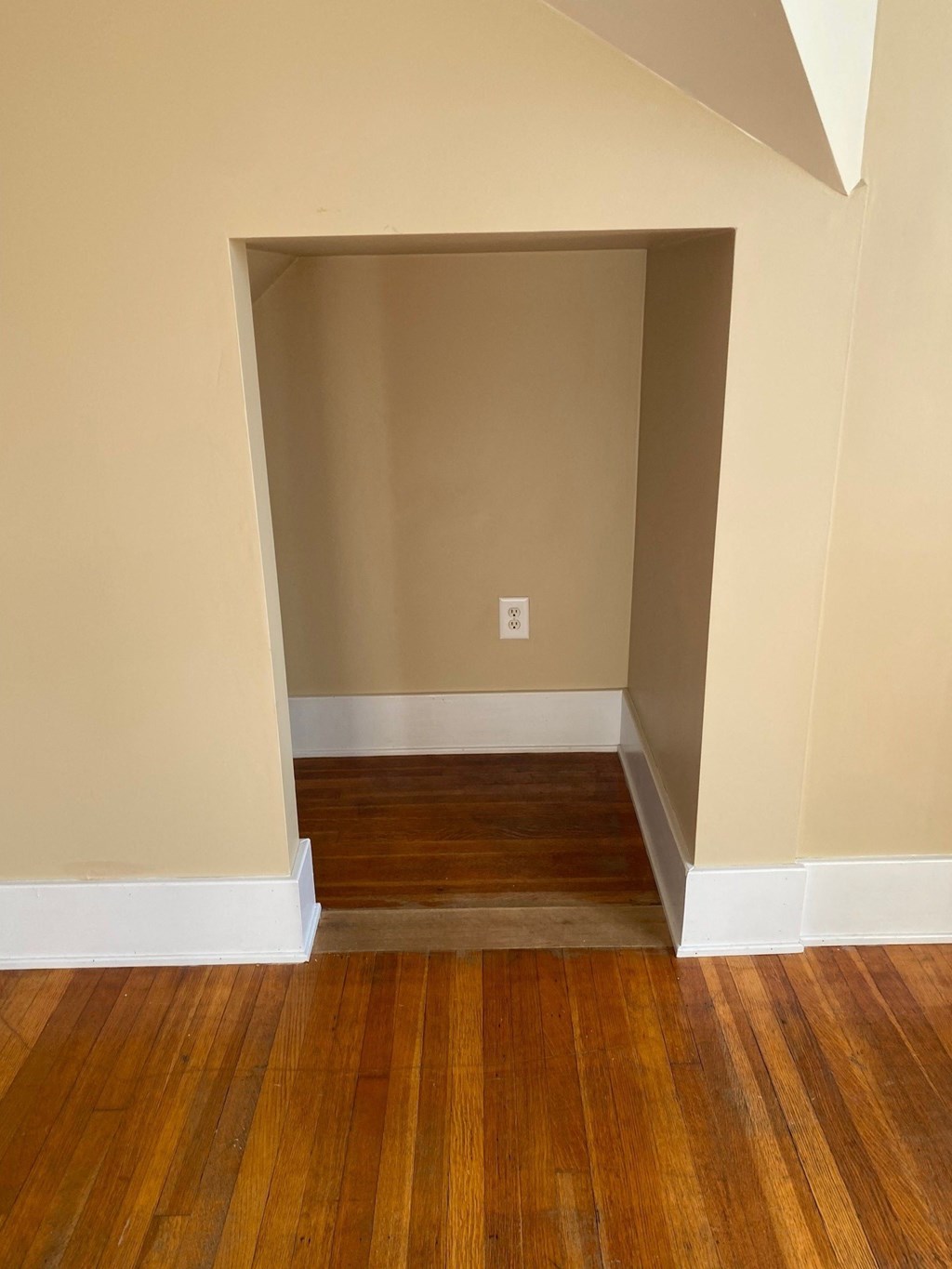 an empty room with wooden floors and beige walls and a door to a room