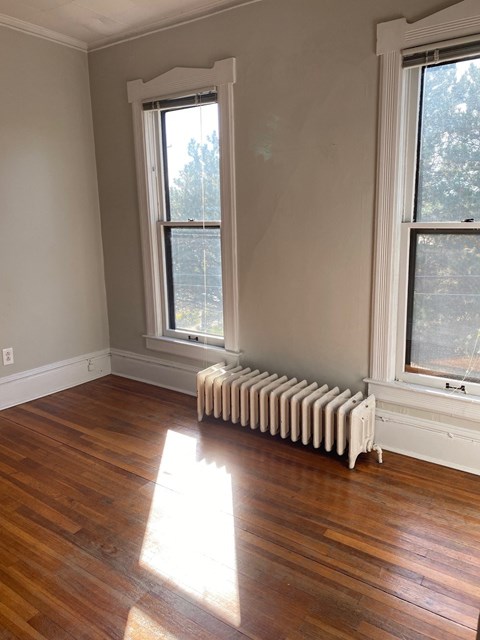 a room with a wood floor and a radiator and two windows
