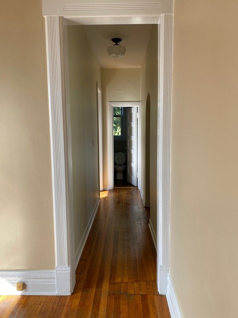 a hallway with wood floors and white walls and a door to a room
