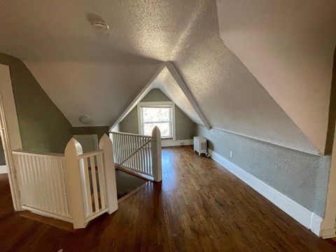 an attic with a staircase and a window and a hard wood floor