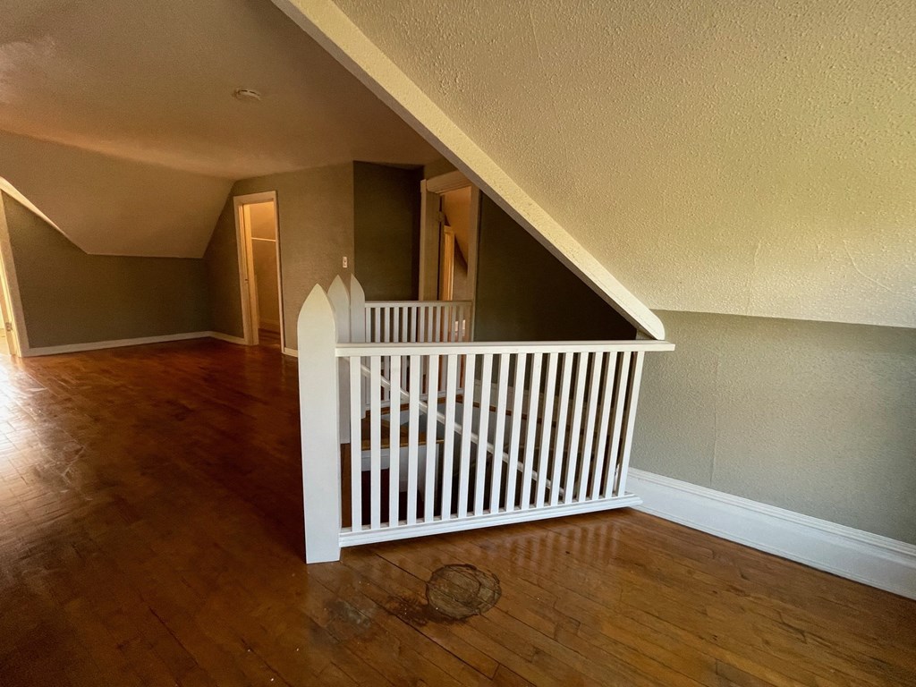 a stairway in an attic with a white railing and a wood floor