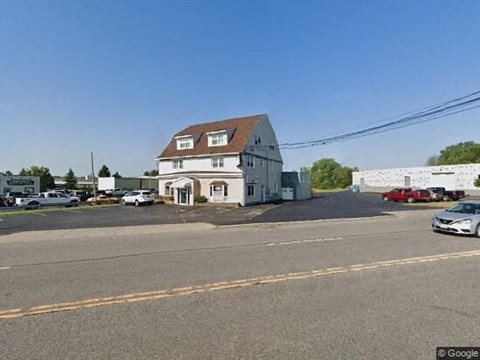 A white building with a brown roof is surrounded by a parking lot.