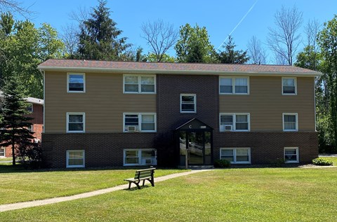 A building with a brown and beige exterior has a covered walkway leading to a door.