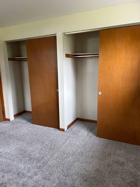 Three brown closet doors in a white room.