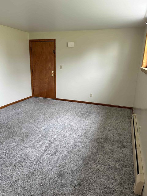 A room with a carpeted floor, a door, and a window with blinds.