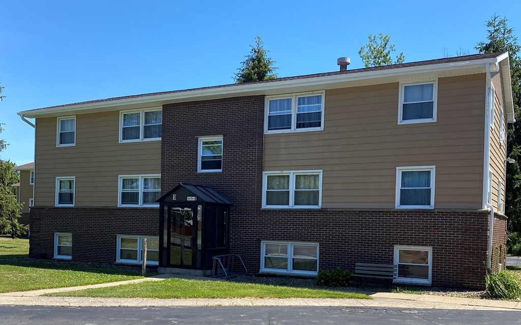 A two-story apartment building with a small entrance and a brick base.