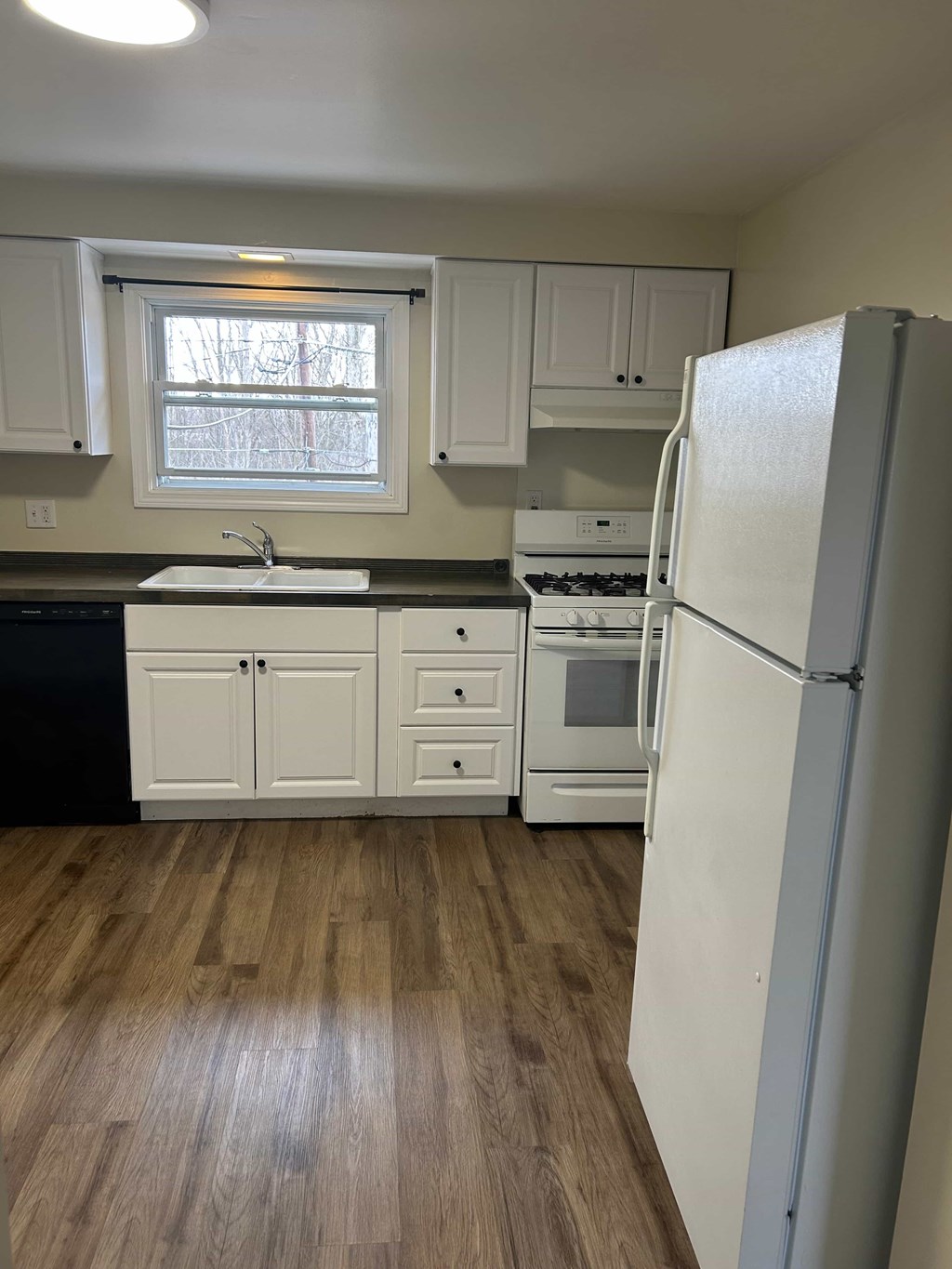 A kitchen with a white fridge, black dishwasher, and white cabinets.