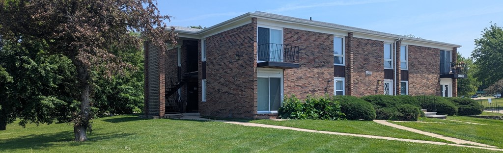 A brick building with a balcony and a tree in front.