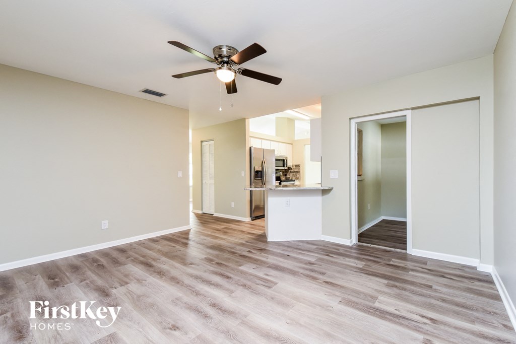 A spacious room with a ceiling fan and light fixture, and a view into another room with a kitchenette.