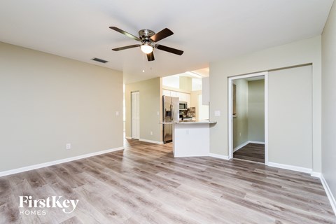 A spacious room with a ceiling fan and light fixture, and a view into another room with a kitchenette.