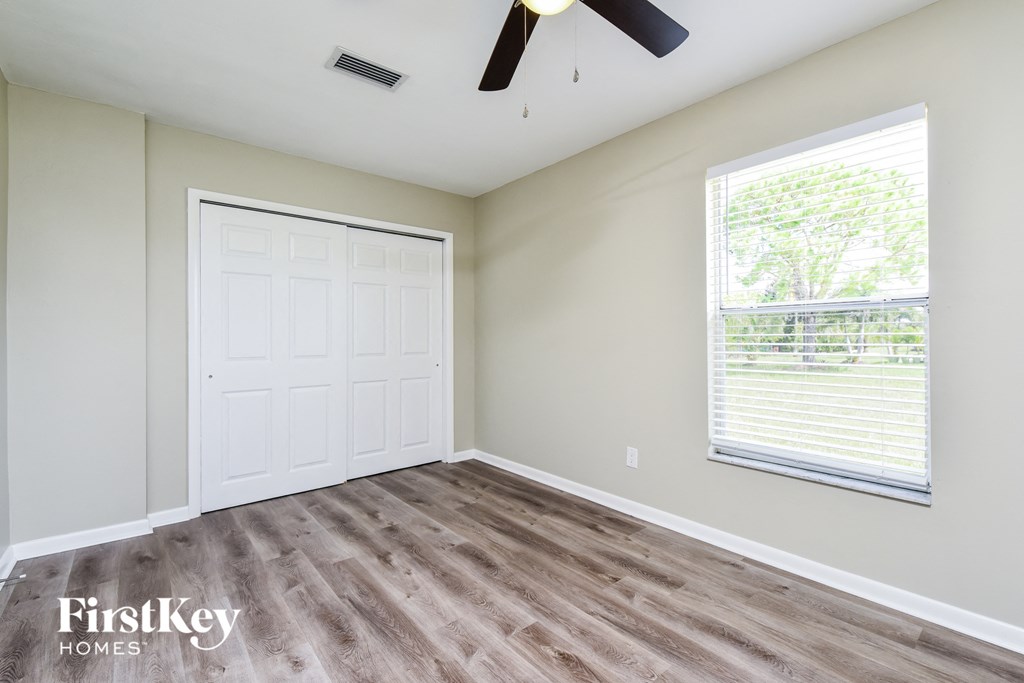 A room with a white door, a ceiling fan, and a window with blinds.
