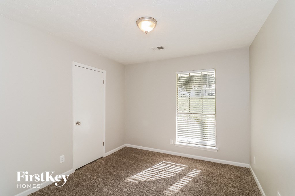 a bedroom with white walls and carpet and a window