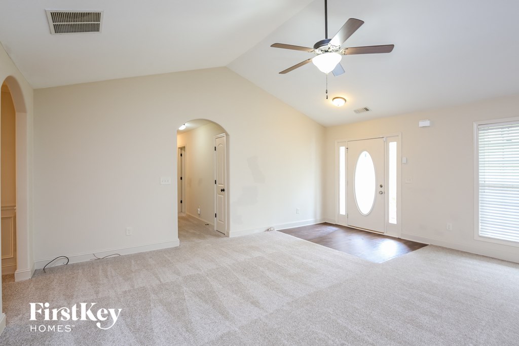 an empty living room with a ceiling fan and a door to a hallway