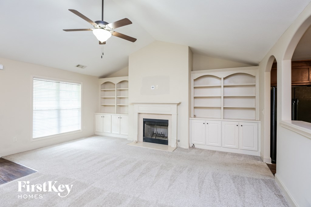 an empty living room with a fireplace and white bookshelves