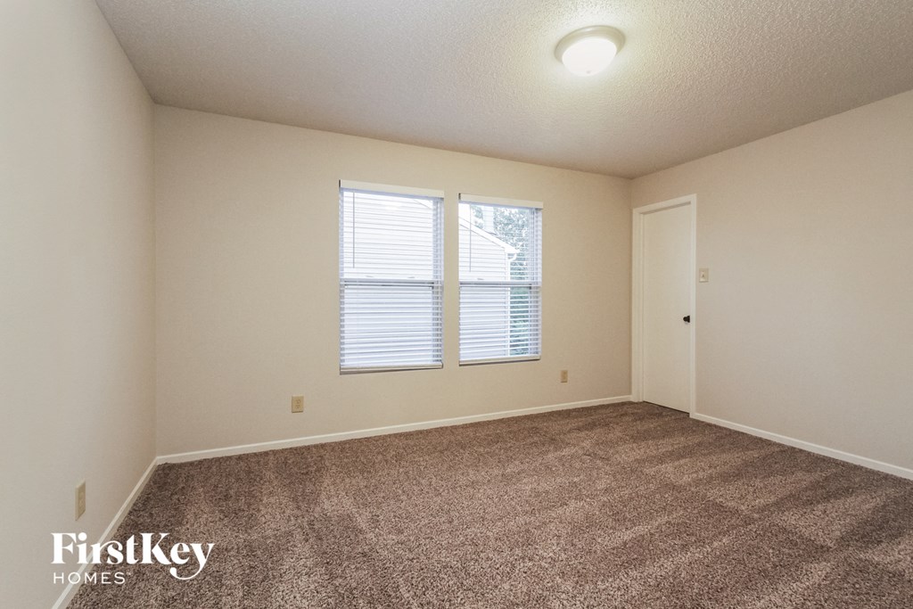 a spacious living room with carpet and two windows