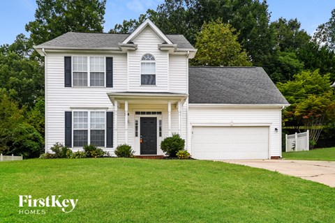 A white house with a black door and windows is surrounded by greenery.