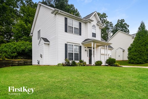 A white house with a black door and windows is surrounded by greenery.