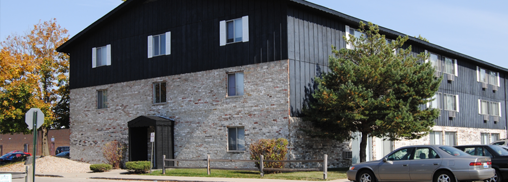 A stone building with a black roof and a tree in front.
