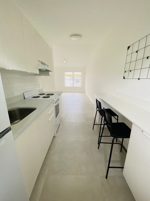 a kitchen with white cabinets and a long counter with black chairs