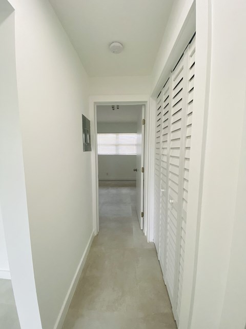 a long hallway with white shutters and a white carpeted floor and a hallway