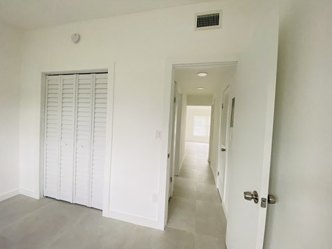a hallway with white walls and white shutters and a white door and a hallway
