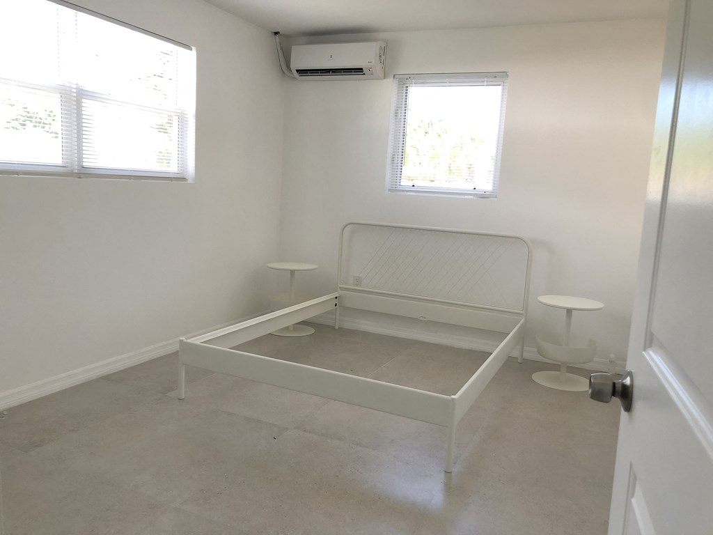 an empty room with a crib in the corner and two windows