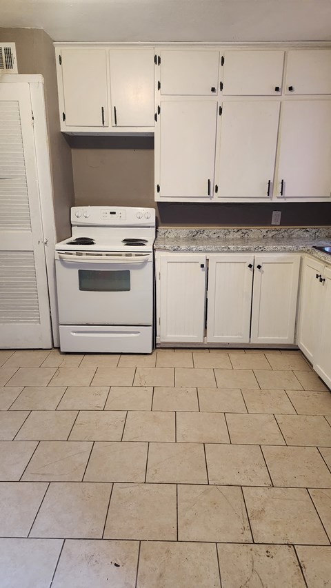 an empty kitchen with white cabinets and a white stove