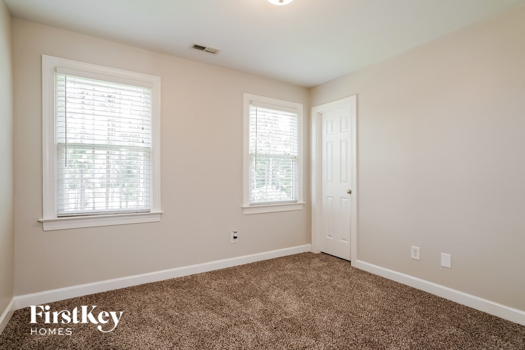 a bedroom with carpet and two windows and a door