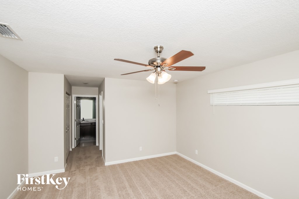 a spacious living room with a ceiling fan and a hallway to a bedroom