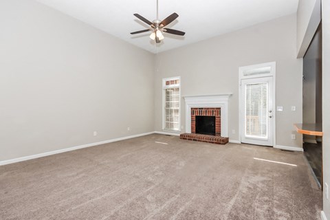 an empty living room with a fireplace and a ceiling fan
