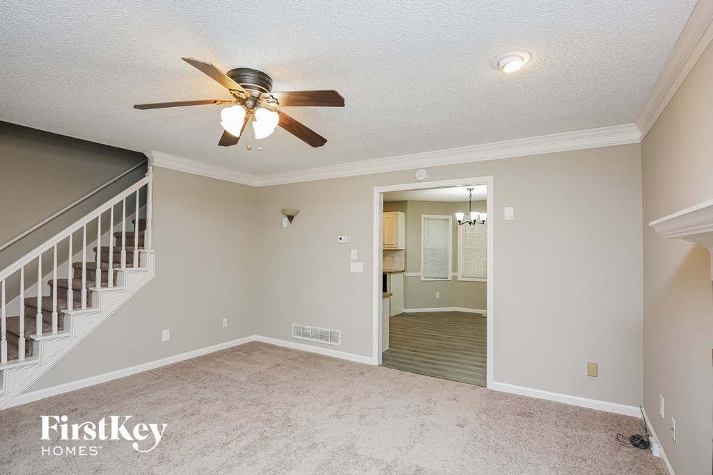 a living room with a ceiling fan and a hallway with a staircase