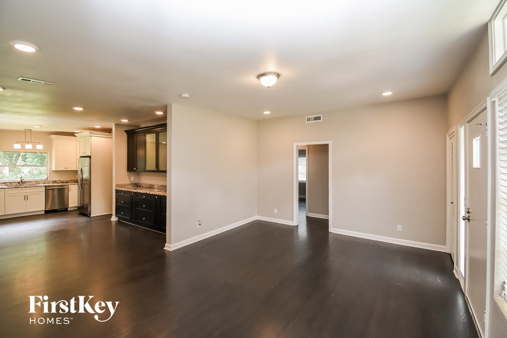 an empty living room with a kitchen in the background