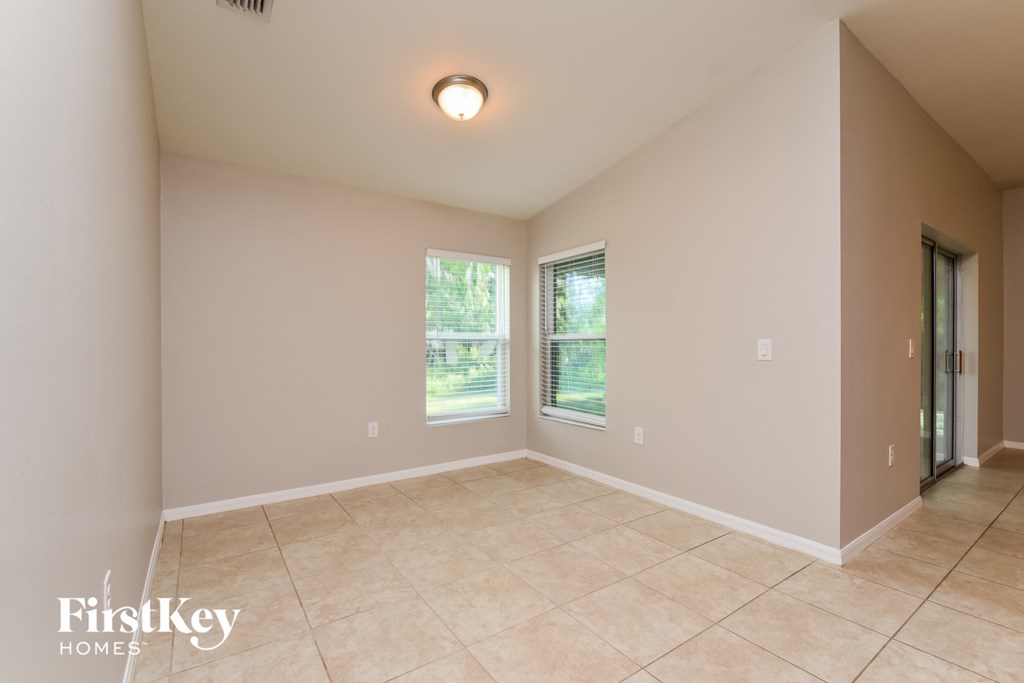 A room with beige walls and tiled flooring, with a window and a door visible.