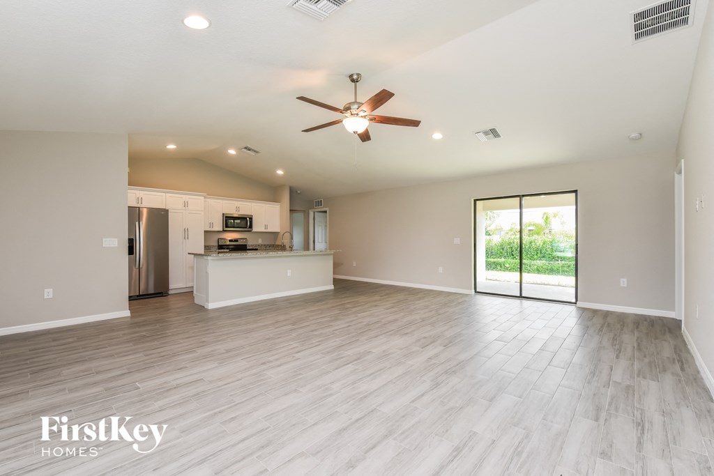 an empty living room with a ceiling fan and a kitchen